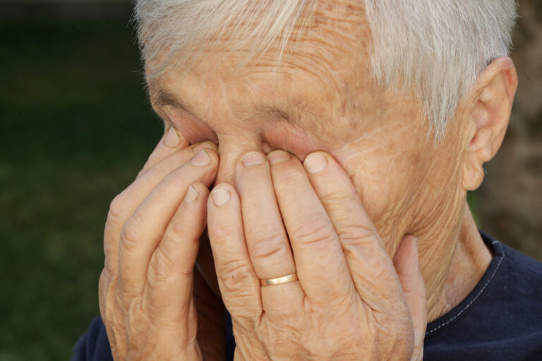 A senior citizen rubs their eyes