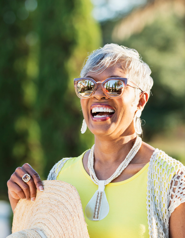 A senior citizen wearing sunglasses smiles in the sunlight