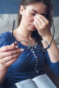 Woman pinching her nose and taking glasses off while reading